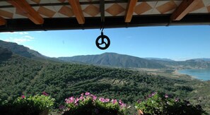 A view from a covered area overlooking a mountainous landscape with a body of water in the distance. - Casa Churchill (Conca de Dalt)