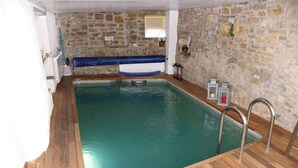 Una piscina interior rectangular con suelo de madera y paredes de piedra.