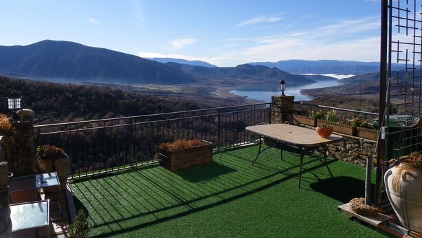Un balcón con vista a un lago y montañas, una mesa y plantas en macetas.