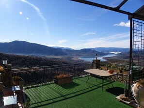 Un balcon donnant sur un lac et des montagnes, avec une table et des plantes en pot.