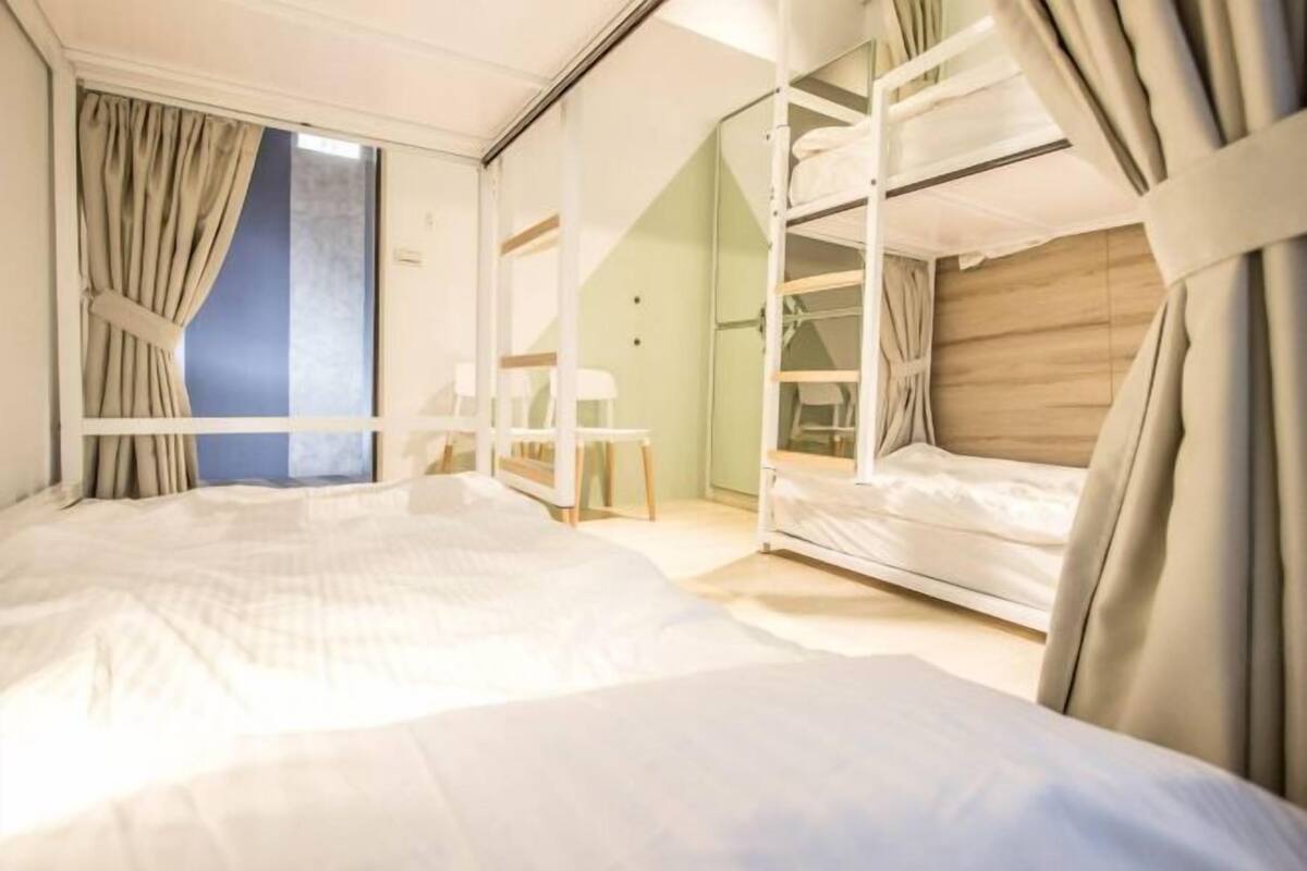 A hotel room with a large bed, bunk beds, a desk, and a window with curtains.