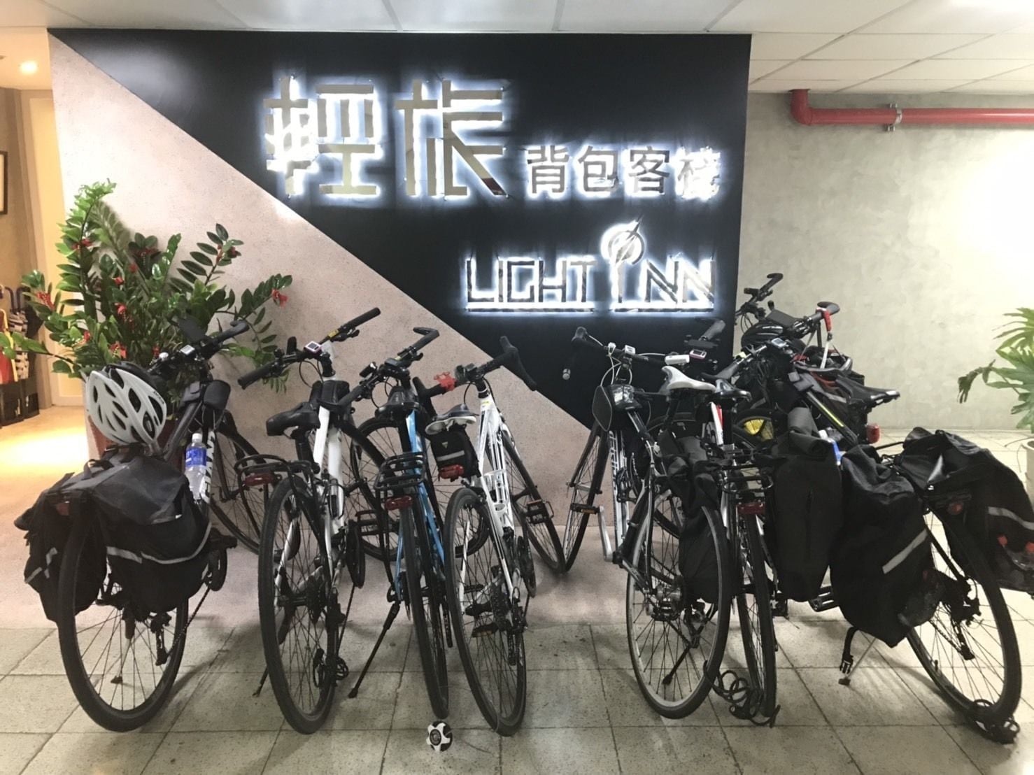A bike rental station with multiple bicycles and helmets, a neon sign with Chinese characters, and potted plants.
