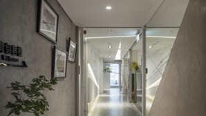 A modern, well-lit hallway with a welcoming sign, framed pictures, and a plant. - LIGHT INN - Hostel (Keelung)