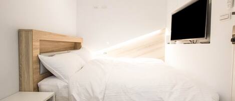 A modern bedroom with a wooden headboard, a flat-screen TV mounted on the wall, and a bedside table.