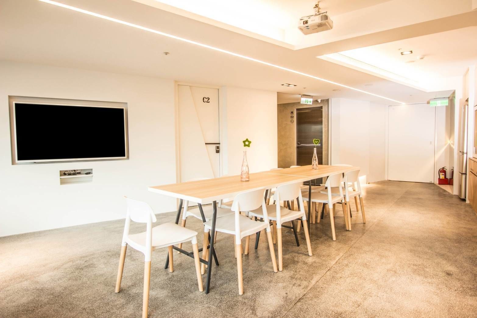 A conference room with a long table, white chairs, a projector, a TV, and a door marked 'C2'.