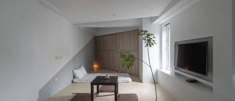 Una sala de estar moderna y minimalista con piso de madera, una mesita baja, un sofá, un televisor grande y una planta en maceta.