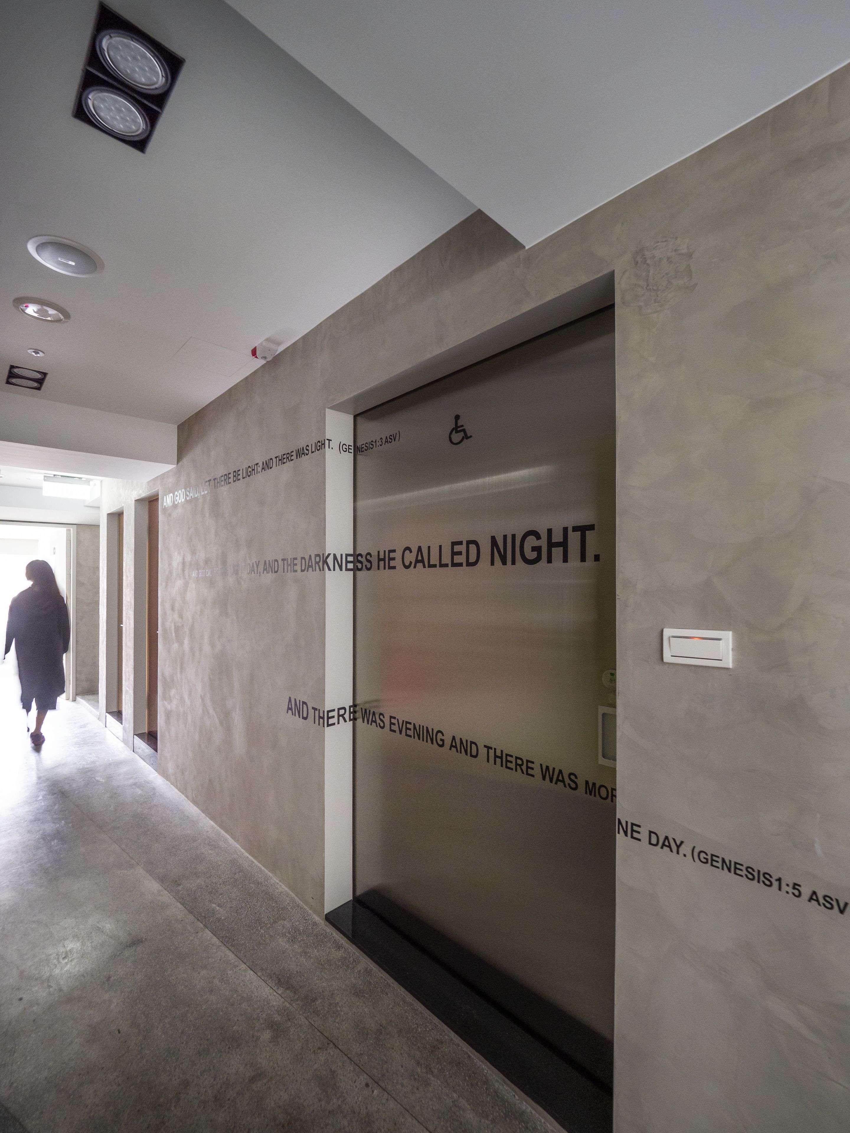 Un pasillo moderno con pared texturizada y una puerta con el símbolo de accesibilidad para sillas de ruedas.