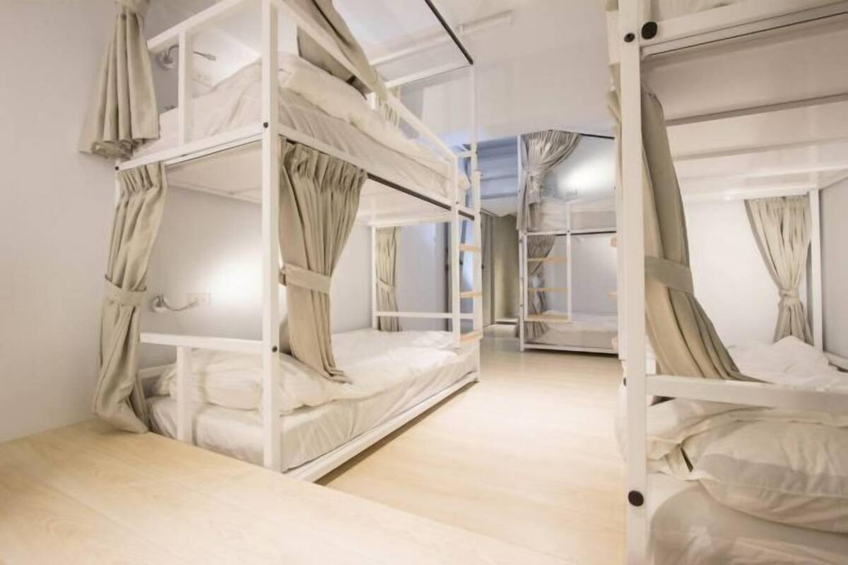 A bunk bed room with curtains, a wooden floor, and a closet with a ladder.