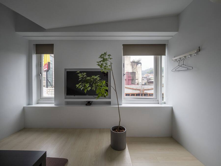 Un salon moderne avec un téléviseur à écran plat posé sur un meuble blanc, une plante en pot et une vue sur le paysage urbain par une fenêtre.