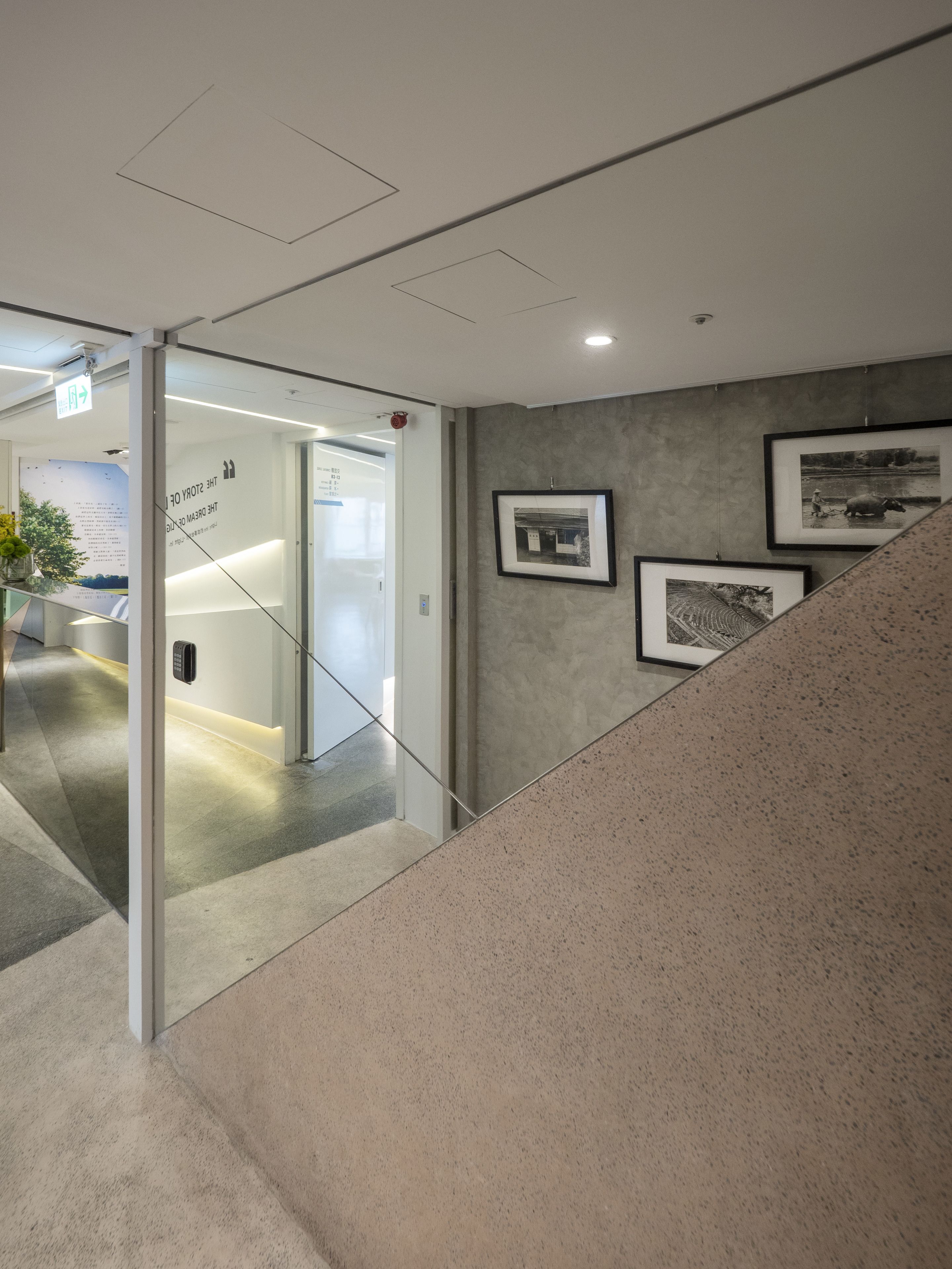 Ein modernes Interieur mit einer Glastür, die zu einem Empfangsbereich führt, einer Treppe und gerahmten Schwarzweißfotos an der Wand.