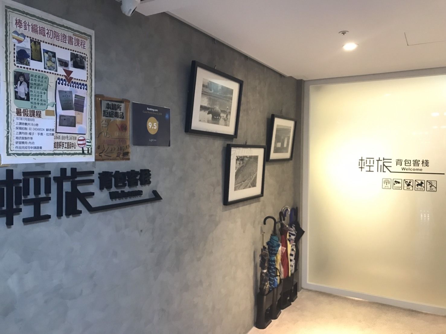Un área de recepción con un letrero en la pared, cuadros enmarcados y un perchero con objetos colgados.