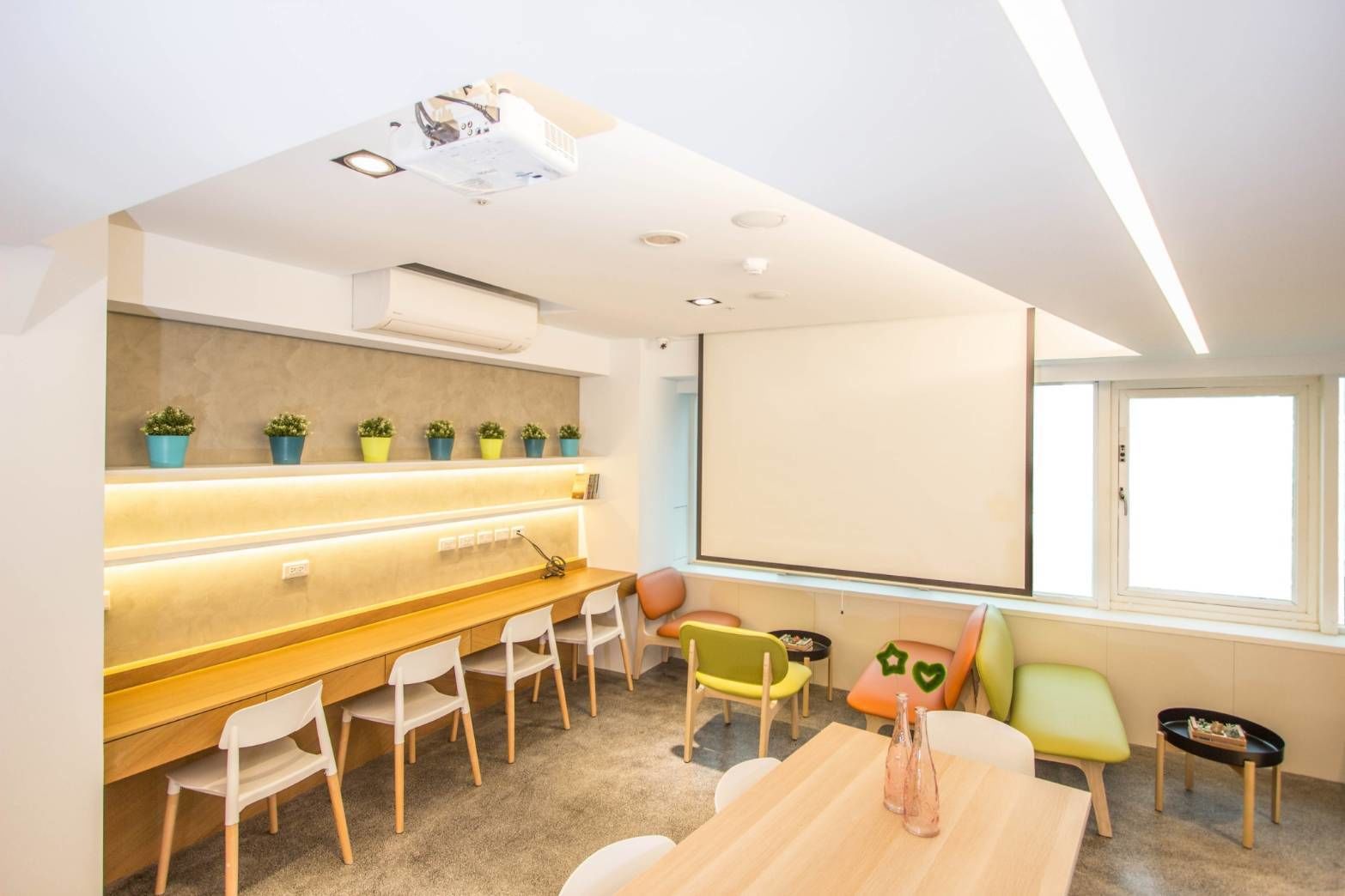 A modern meeting room with a long table, white chairs, a projector screen, and potted plants.