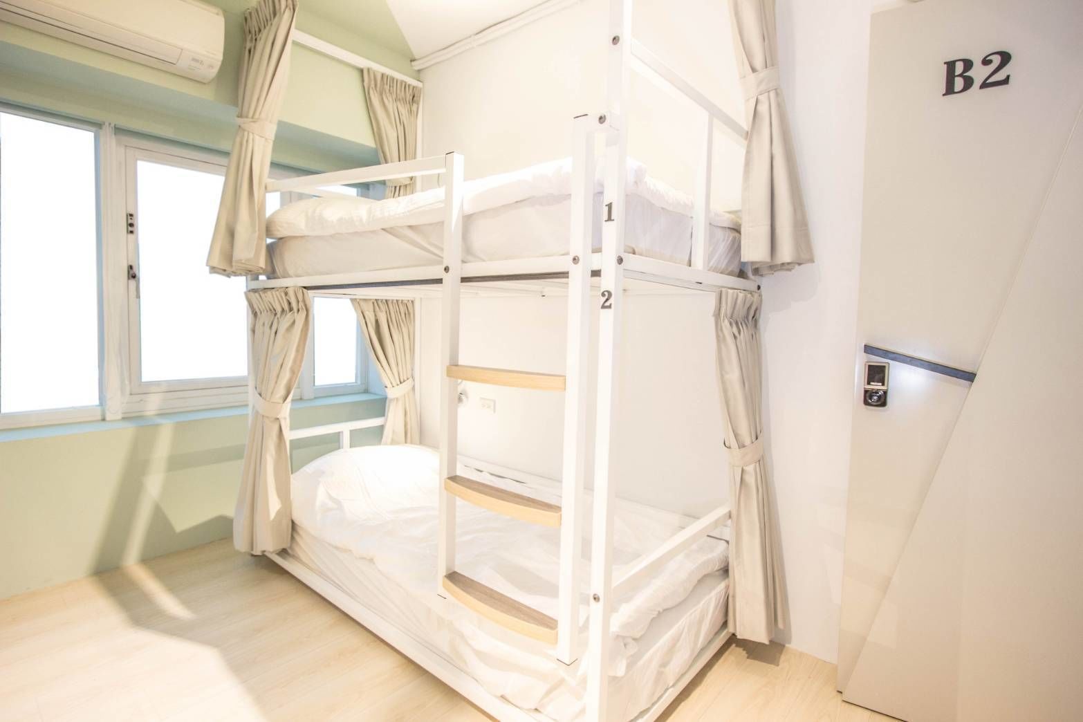 A bunk bed room with a window, curtains, and a door labeled B2.