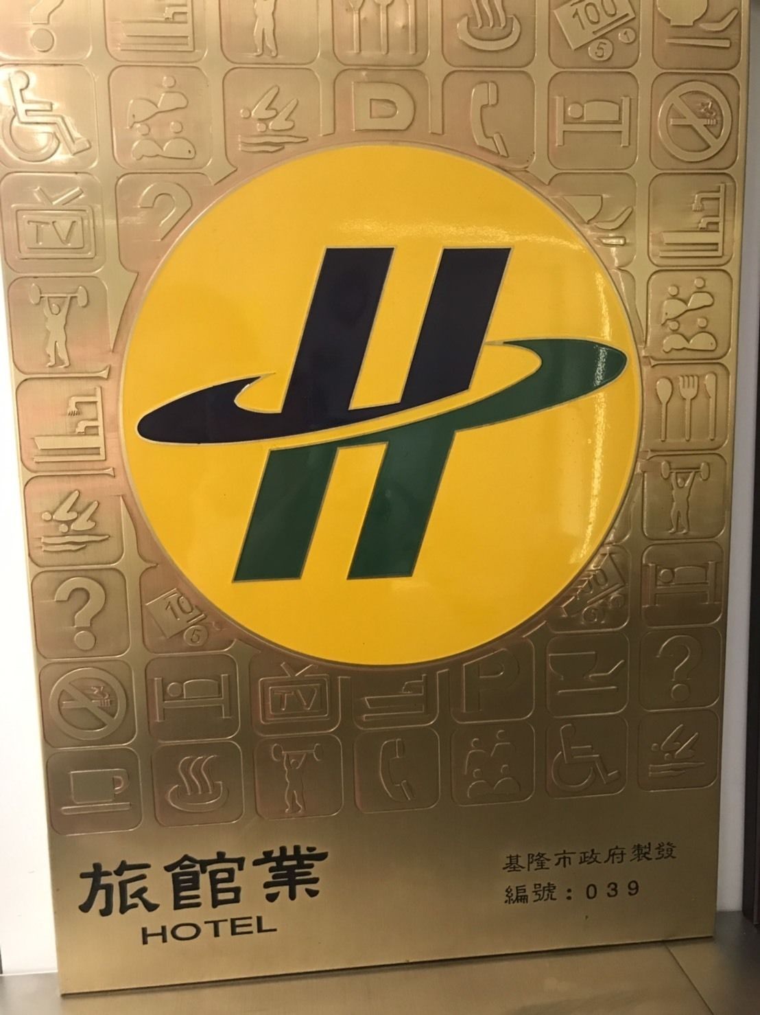 A hotel sign with a large yellow and green logo, surrounded by various icons indicating amenities such as TV, dining, and parking.