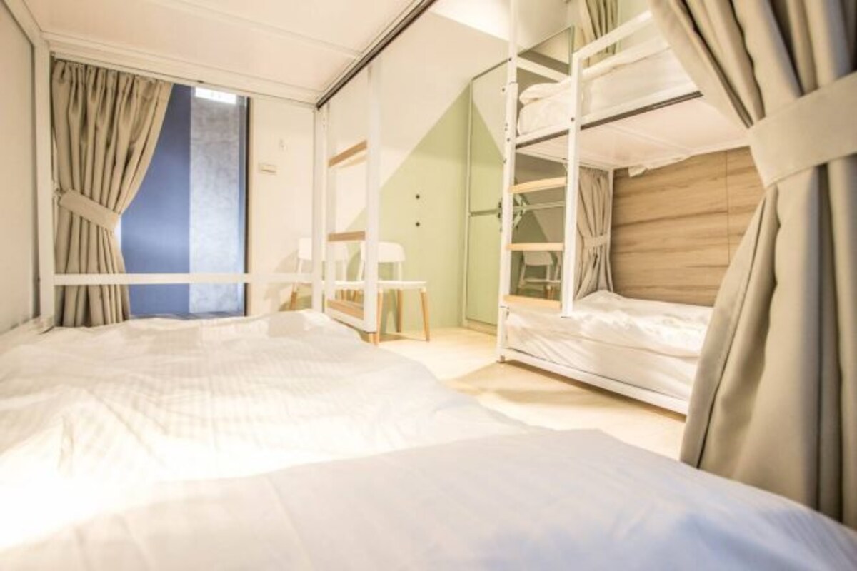 A hotel room with a large bed, bunk beds, a desk, and a window with curtains.