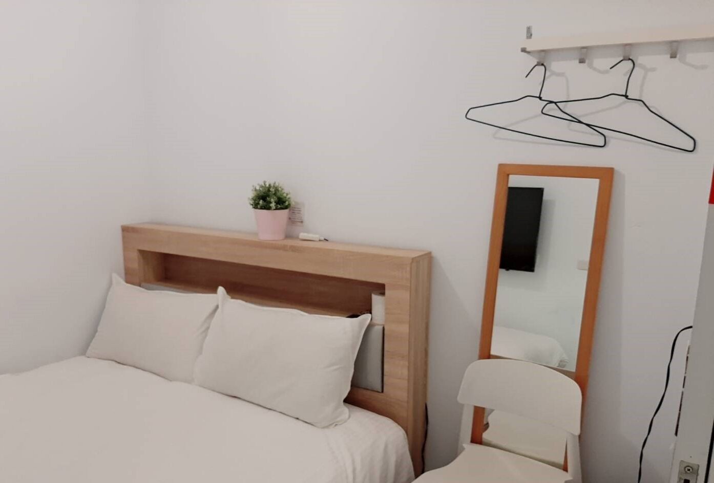 Une chambre à coucher avec une tête de lit en bois, un lit avec une literie blanche, une petite plante en pot, un miroir et un porte-vêtements.