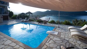 Una piscina con baldosas de piedra, sillas de descanso y vistas a un lago y montañas.