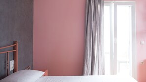 Un dormitorio con cama, cabecera de madera, mesita de noche, ventana con cortinas y una puerta.