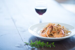 A plate of pasta with shrimp on a wooden table with a glass of red wine in the background.