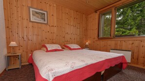 Ein Schlafzimmer mit Holzwänden, zwei Betten, einem gerahmten Bild an der Wand und einem Fenster mit Blick auf Bäume.