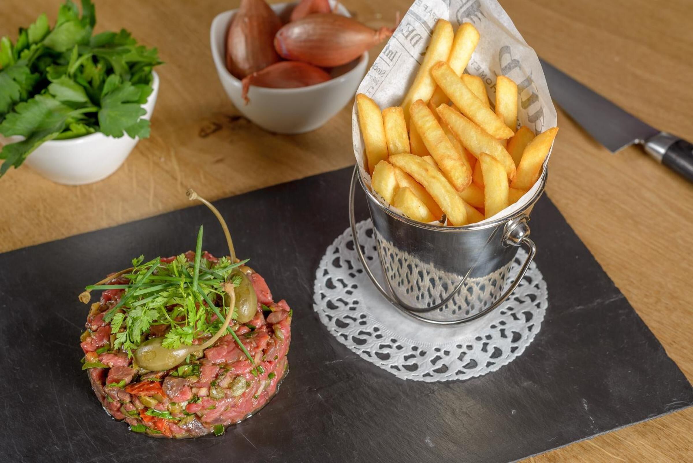Un plat de steak tartare accompagné de frites et d’oignons.
