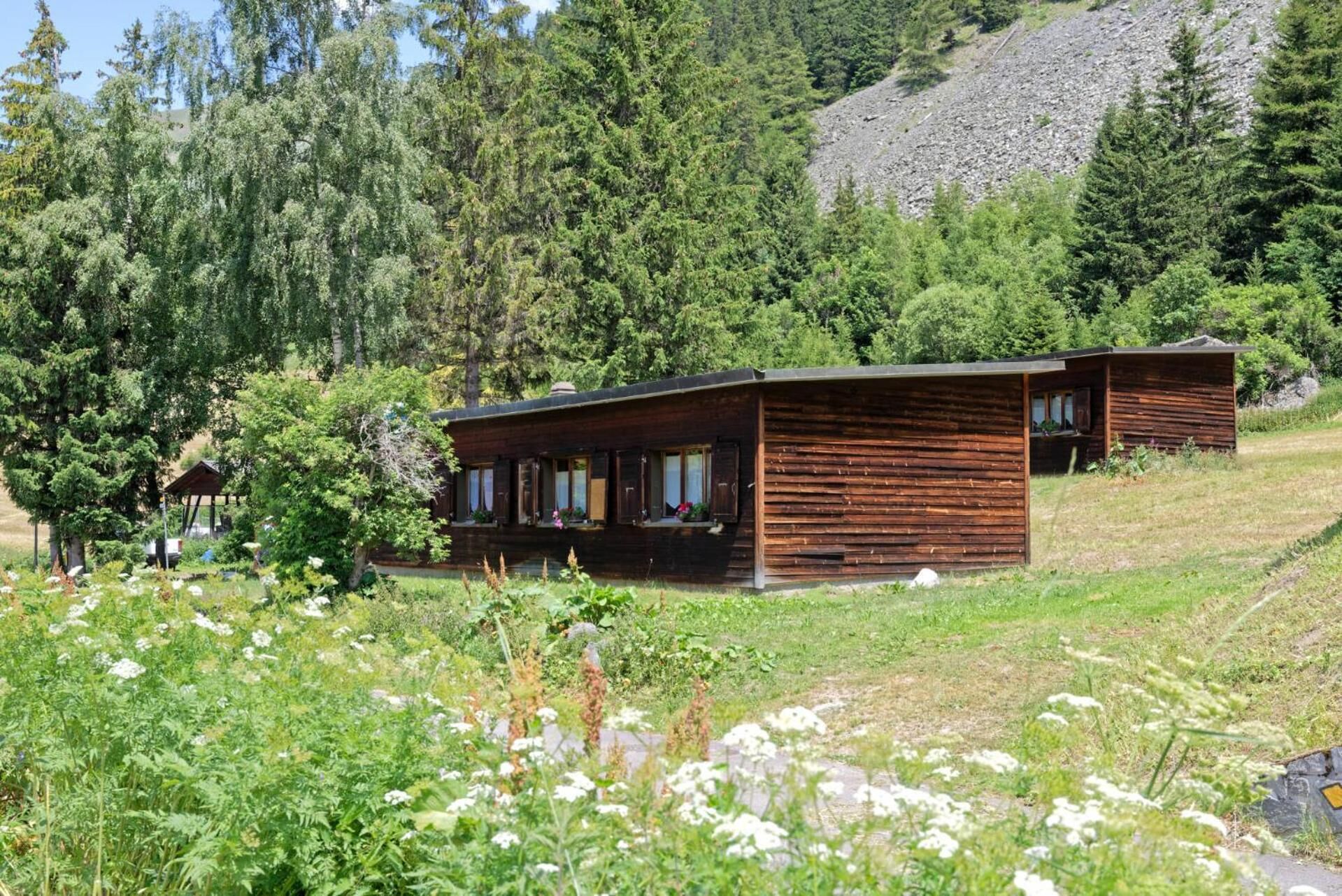 En hytte med træfacade, omgivet af frodig vegetation og en klippebakkeskråning.