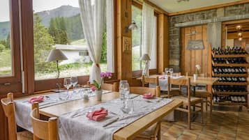 Un comedor con mesas y sillas de madera, una estantería para vinos y vistas al exterior.