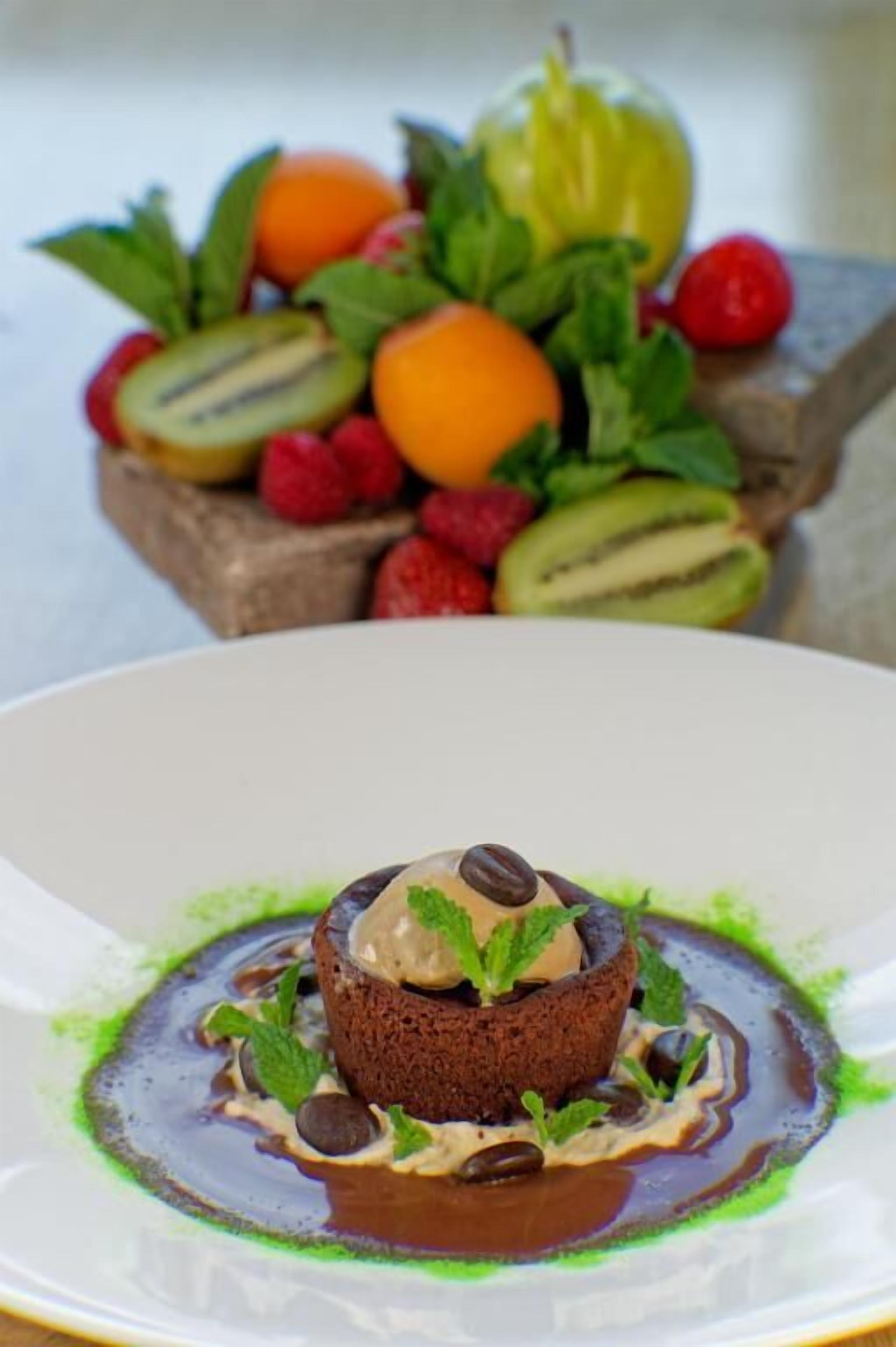 A dessert on a plate with a fruit arrangement in the background.