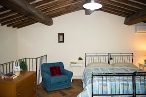 A bedroom with a bed, a chair, a small table, and a wooden dresser. - B&B Il Fienile (San Gimignano)