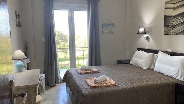 Habitación de hotel con una cama grande, una mesita de noche con lámpara, vistas por la ventana y una obra de arte colgada en la pared.