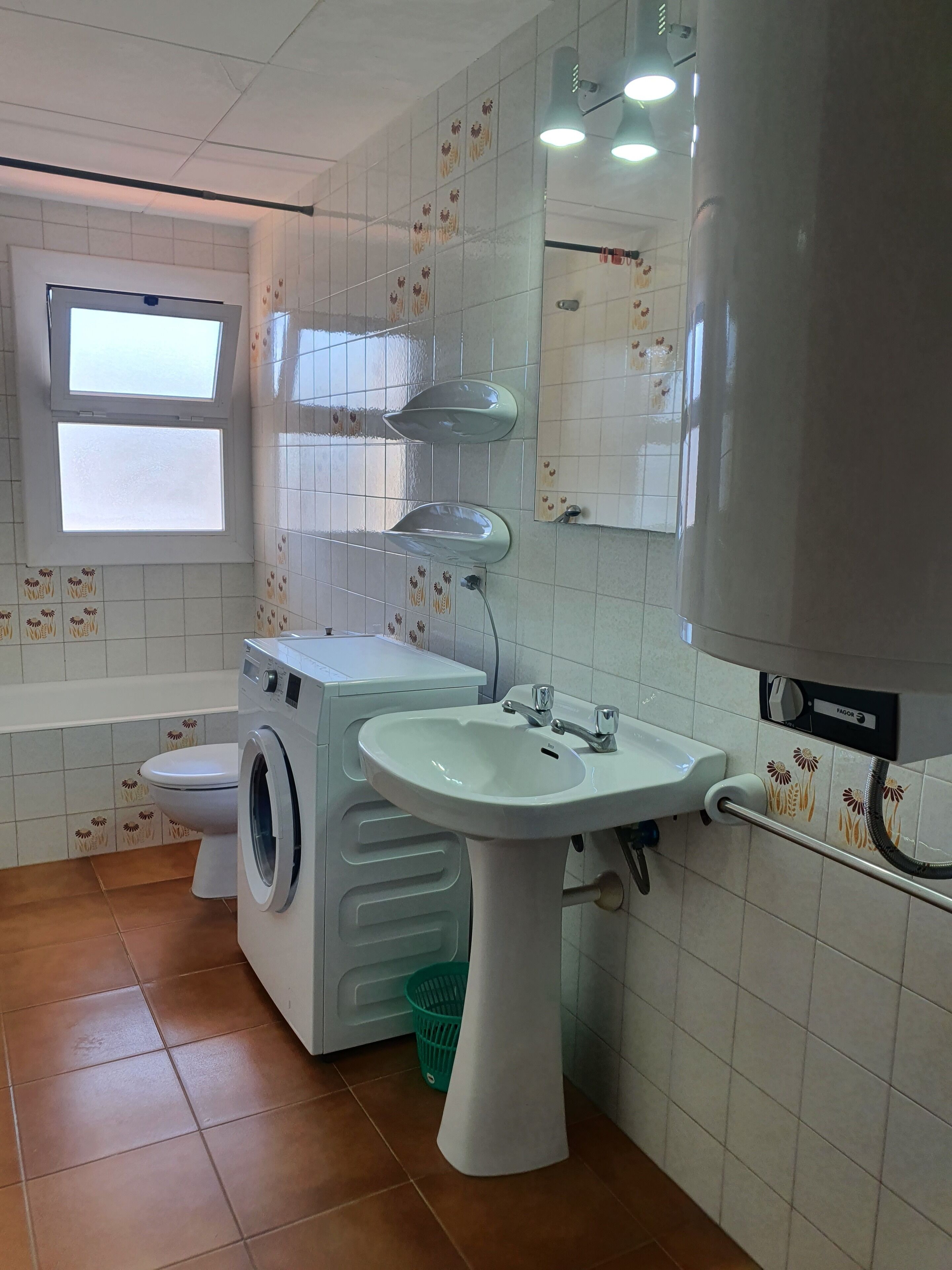Un baño con lavadora, lavamanos, inodoro y ventana.