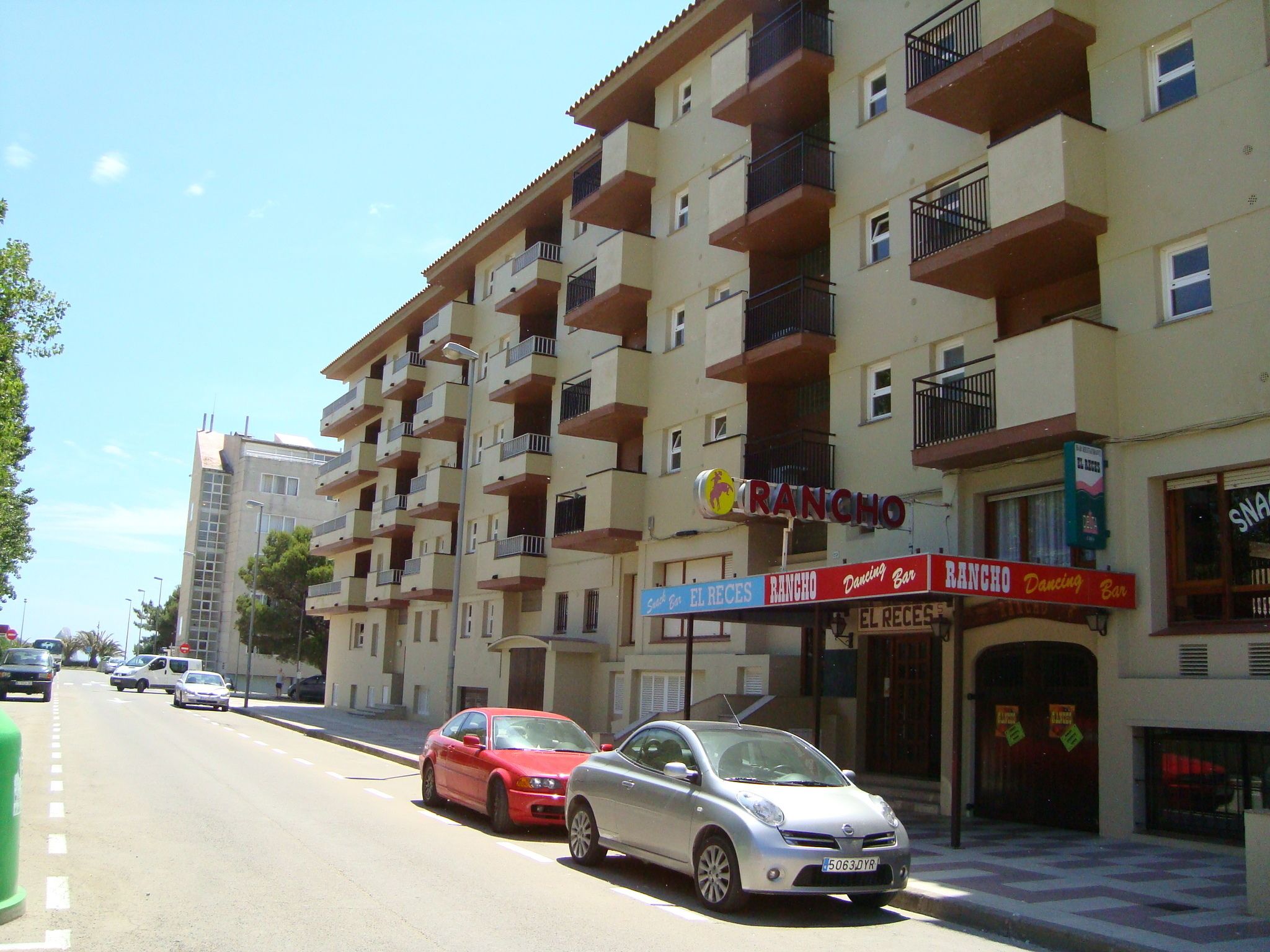 A multi-story building with balconies, a red car parked in front, and a sign for 'RANCHO Dancing Bar'.