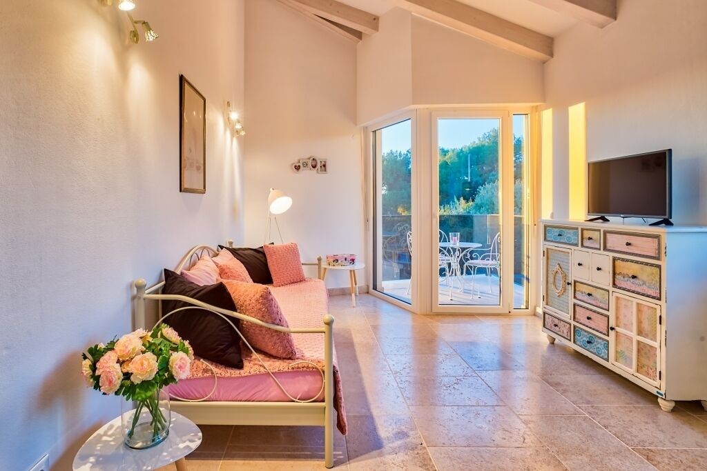A bedroom with a bed, bedside table, lamp, dresser, TV, and a view of the outdoors.
