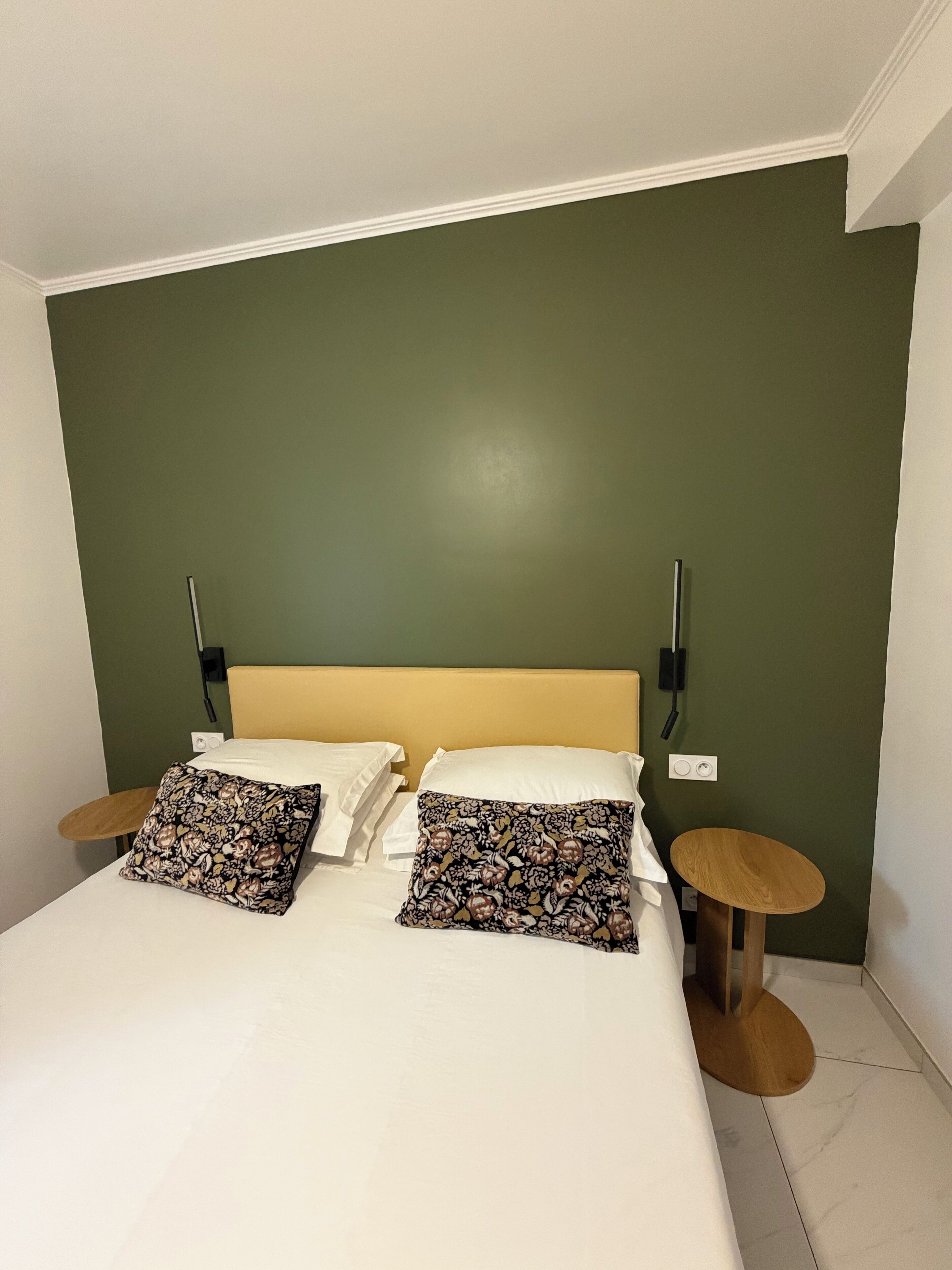 Una cama con dos almohadas, un cabecero de madera, dos mesitas de noche y una pared verde.