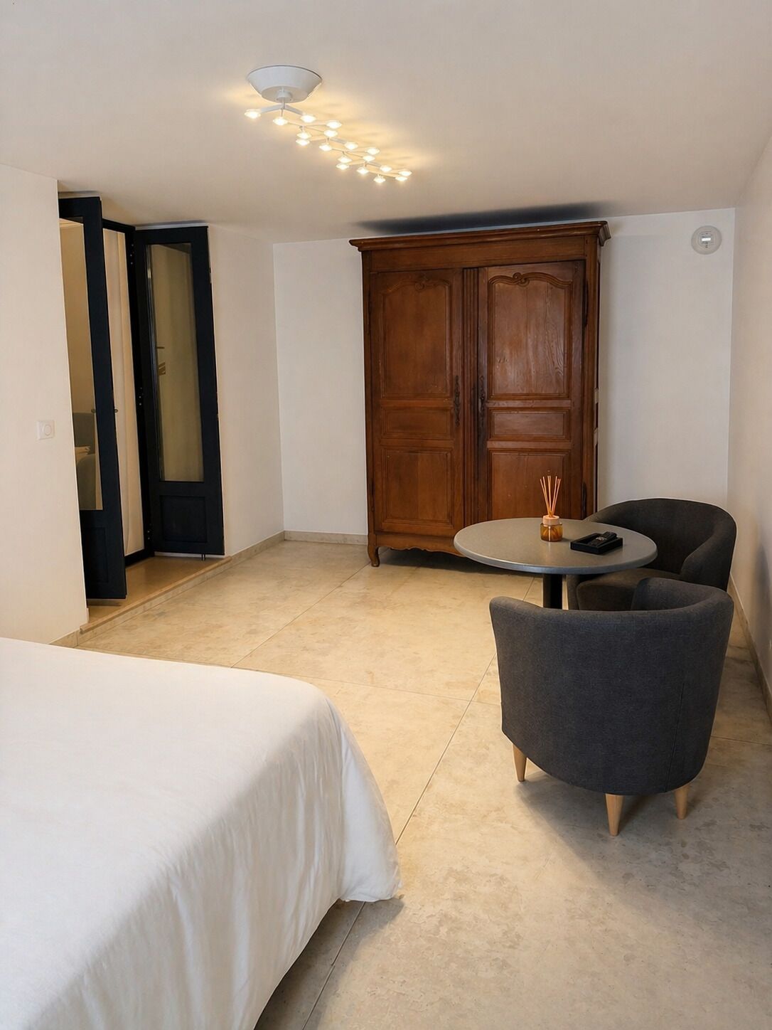 Una habitación con una cama, una mesa redonda con dos sillas, un armario de madera y una lámpara en el techo.