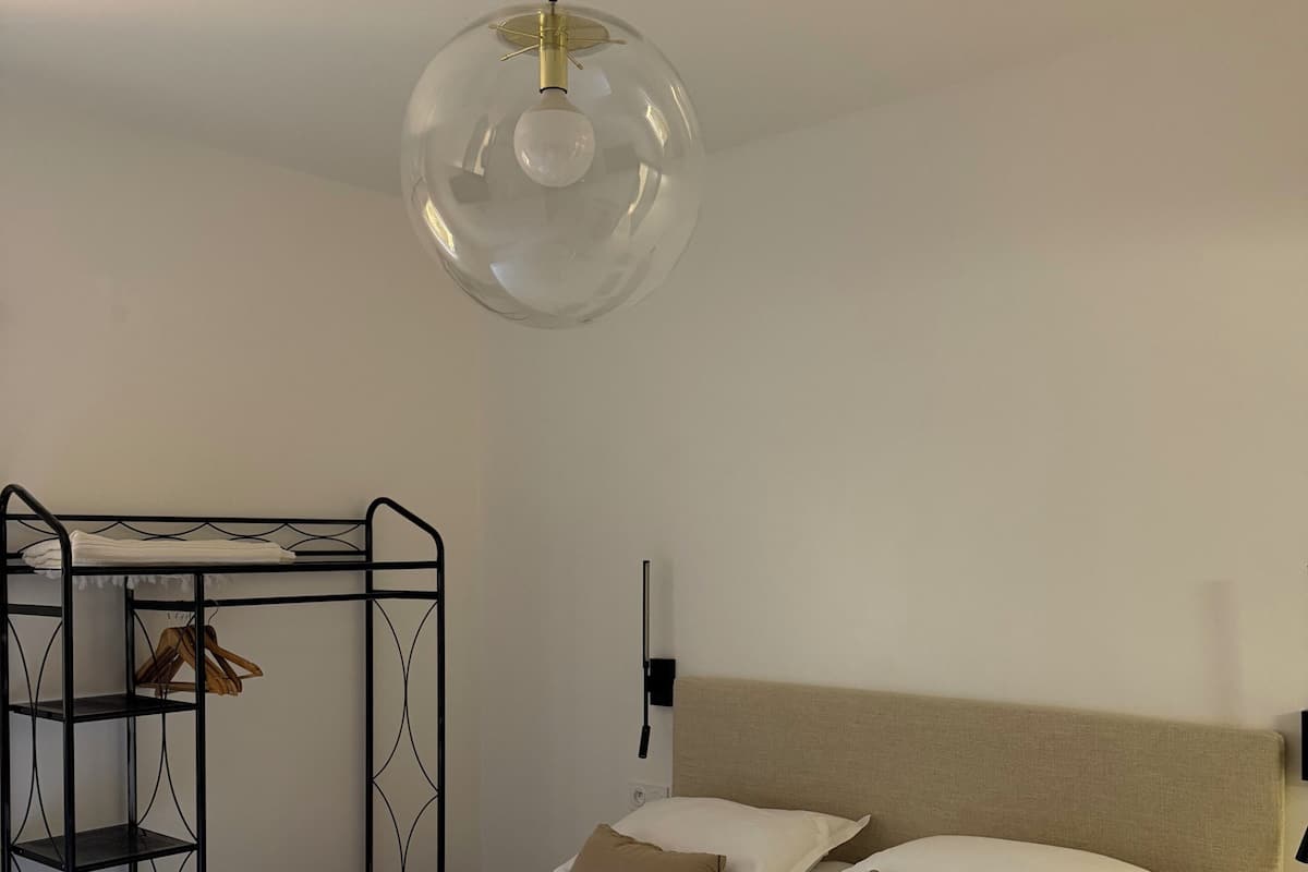 A neatly arranged bedroom with a bed, a hanging light fixture, and a metal shelf unit.