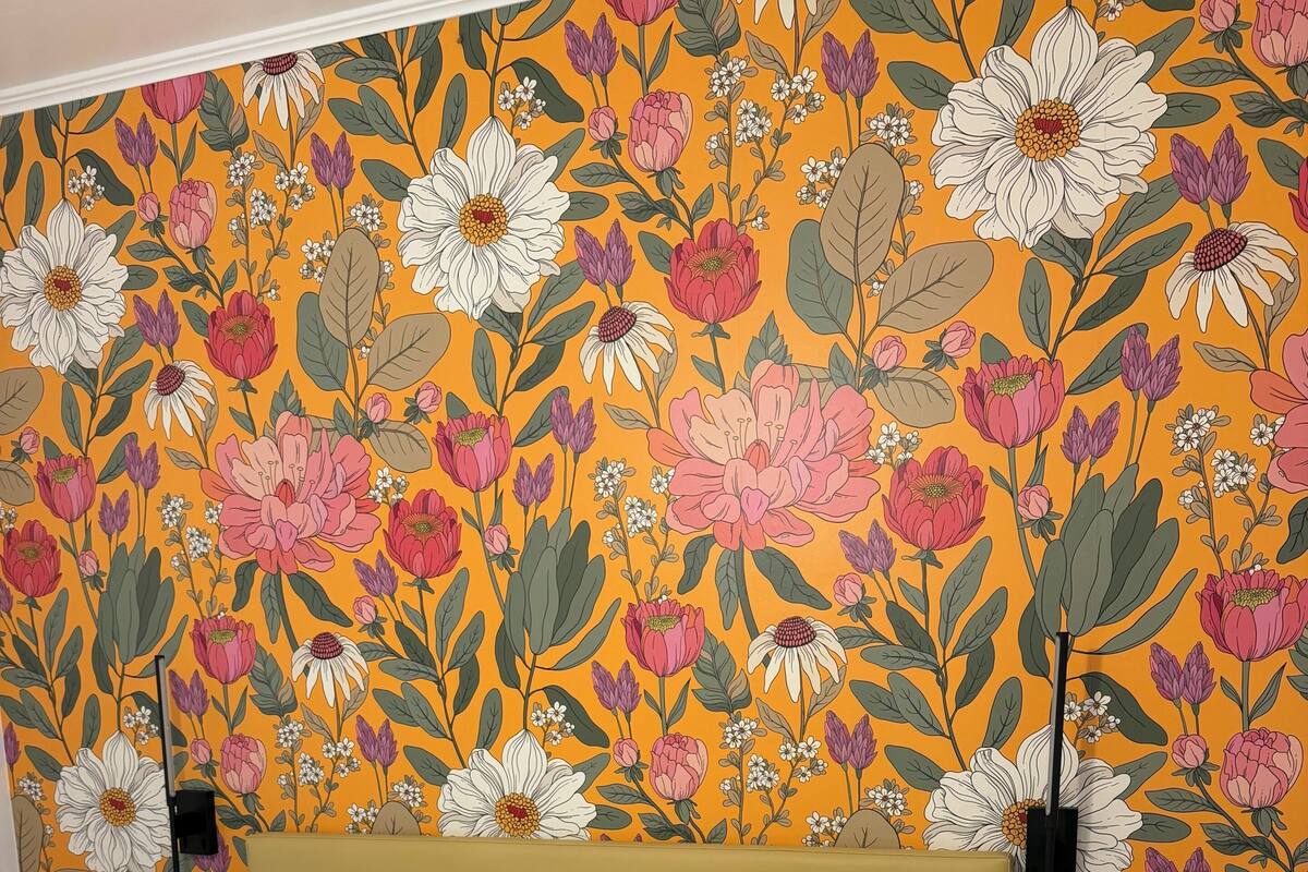 A bed with white and purple bedding, a yellow headboard, and a floral wallpaper pattern.