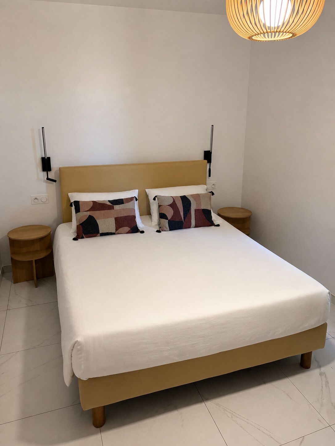 Un lit avec une tête de lit en bois, deux tables de chevet et un luminaire suspendu.