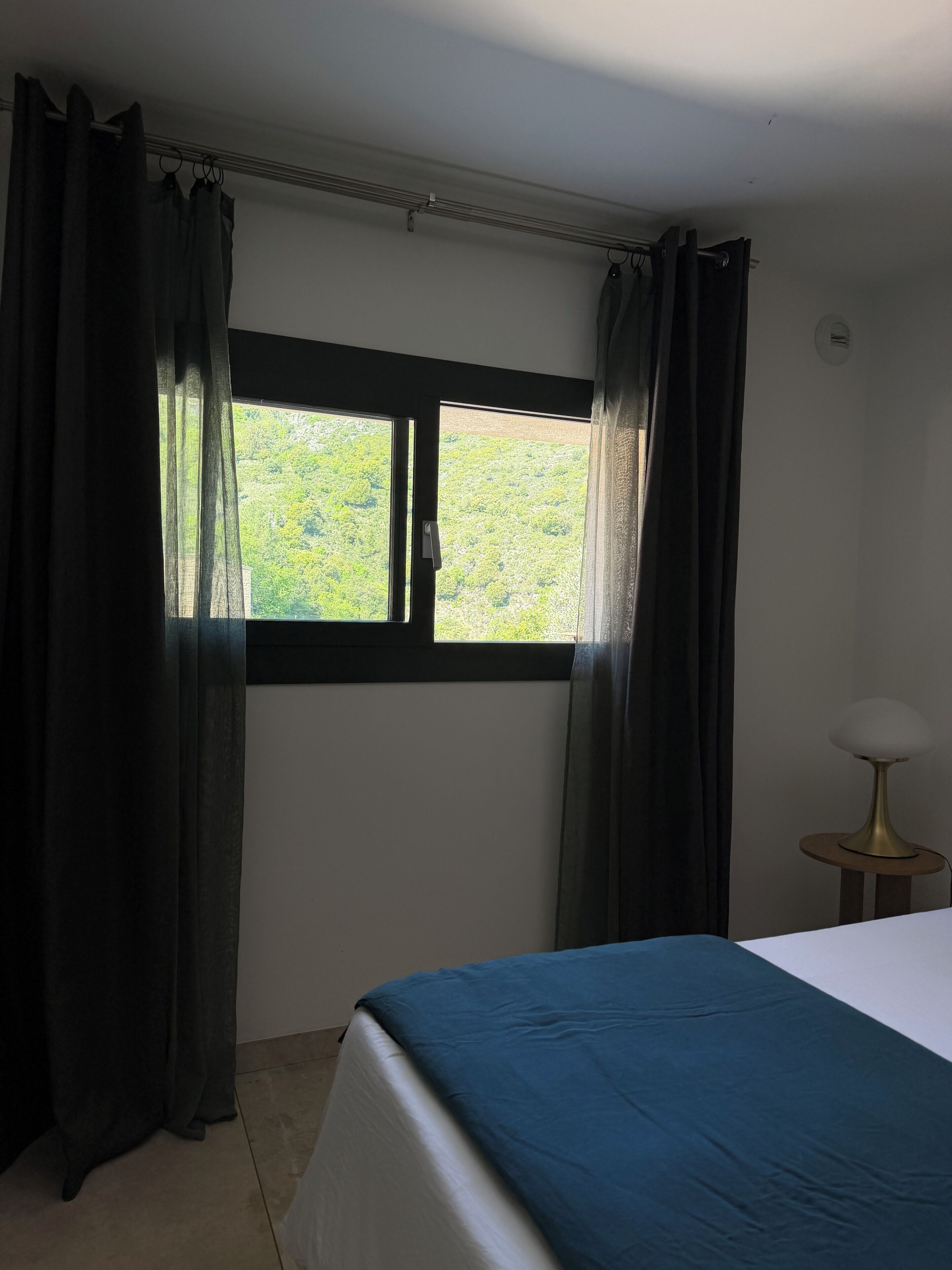 Une chambre à coucher avec un lit, une fenêtre avec des rideaux et une petite table avec une lampe.