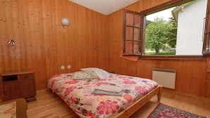 Ein Schlafzimmer mit Holzwänden, einem Bett, einem Nachttisch, einem Schreibtisch und einem Fenster mit Blick auf Bäume.