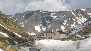 Eine Berghütte mit einer Straße, die zu einer Küstenregion führt, umgeben von schneebedeckten Berggipfeln.