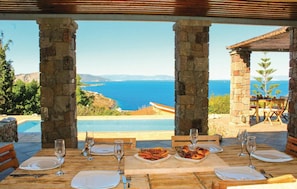 A dining table set with plates, cutlery, and glasses, overlooking a pool and the sea. - Beach front home in Perdika (Perdika)