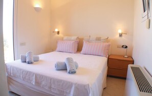 A neatly made bed with two pillows, a bedside table with a lamp, and a wall-mounted light fixture. - Beach front home in Perdika (Perdika)