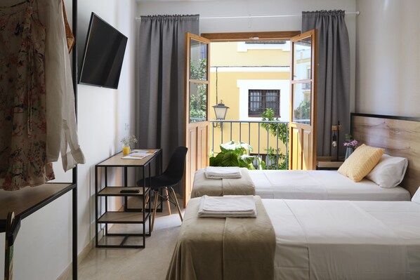 A hotel room with two beds, a desk, a chair, a TV, and a balcony with plants. - Sweet Sevilla Suites - Smart Hotel (Seville)