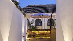 A narrow wooden pathway leading to a seating area with a white wall and a tiled roof in the background. - Sweet Sevilla Suites - Smart Hotel (Seville)