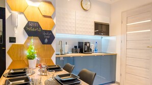 A modern kitchen with a built-in microwave, coffee maker, and a small refrigerator. There is a dining area with a wooden table set for two, and a potted plant on the wall. - Izerska Przygoda - Apartamenty 5d (Swieradow-Zdroj)