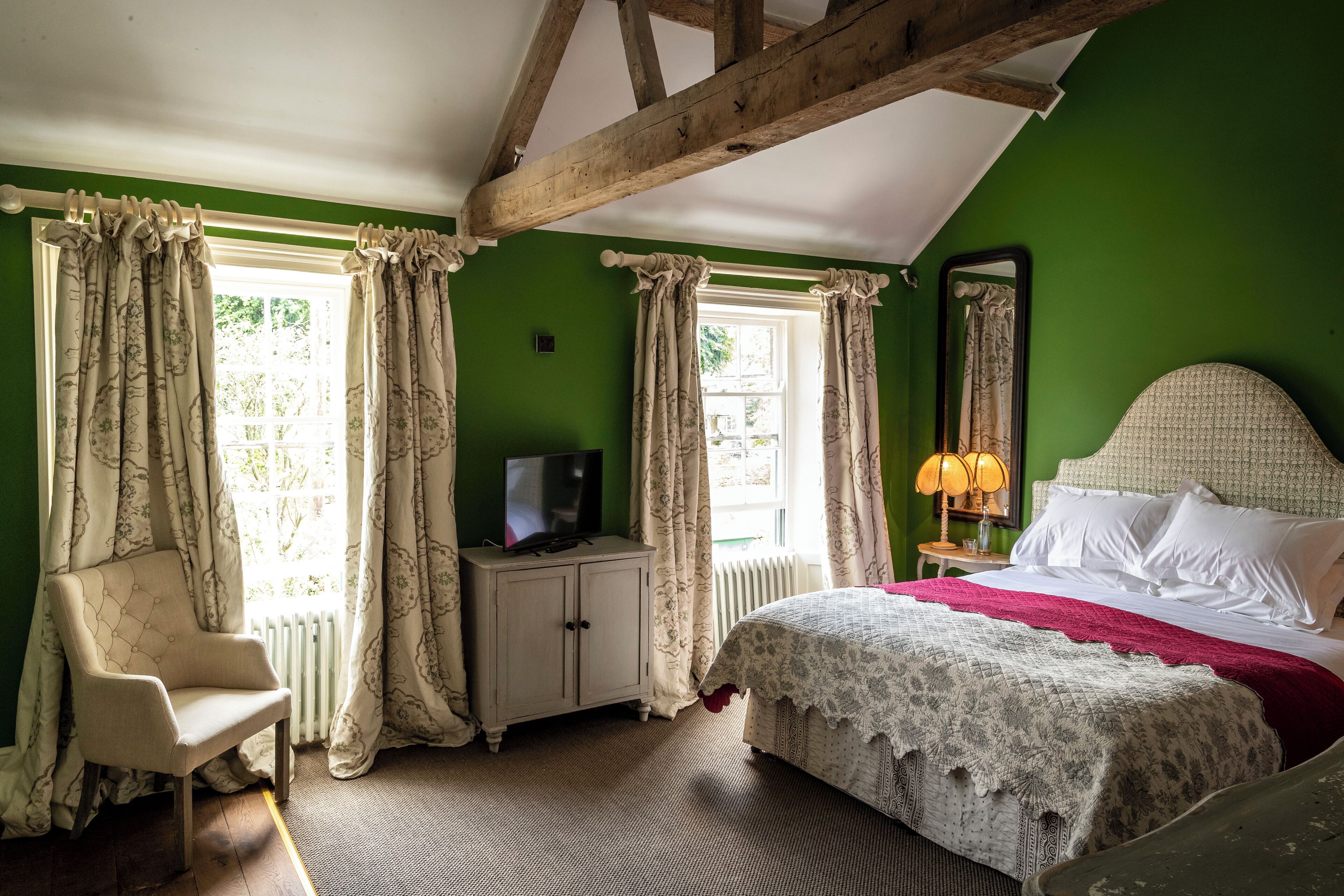 A bedroom with a bed, a chair, a television on a cabinet, and a window with curtains.