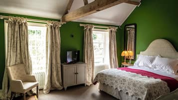 A bedroom with a bed, a chair, a television on a cabinet, and a window with curtains.