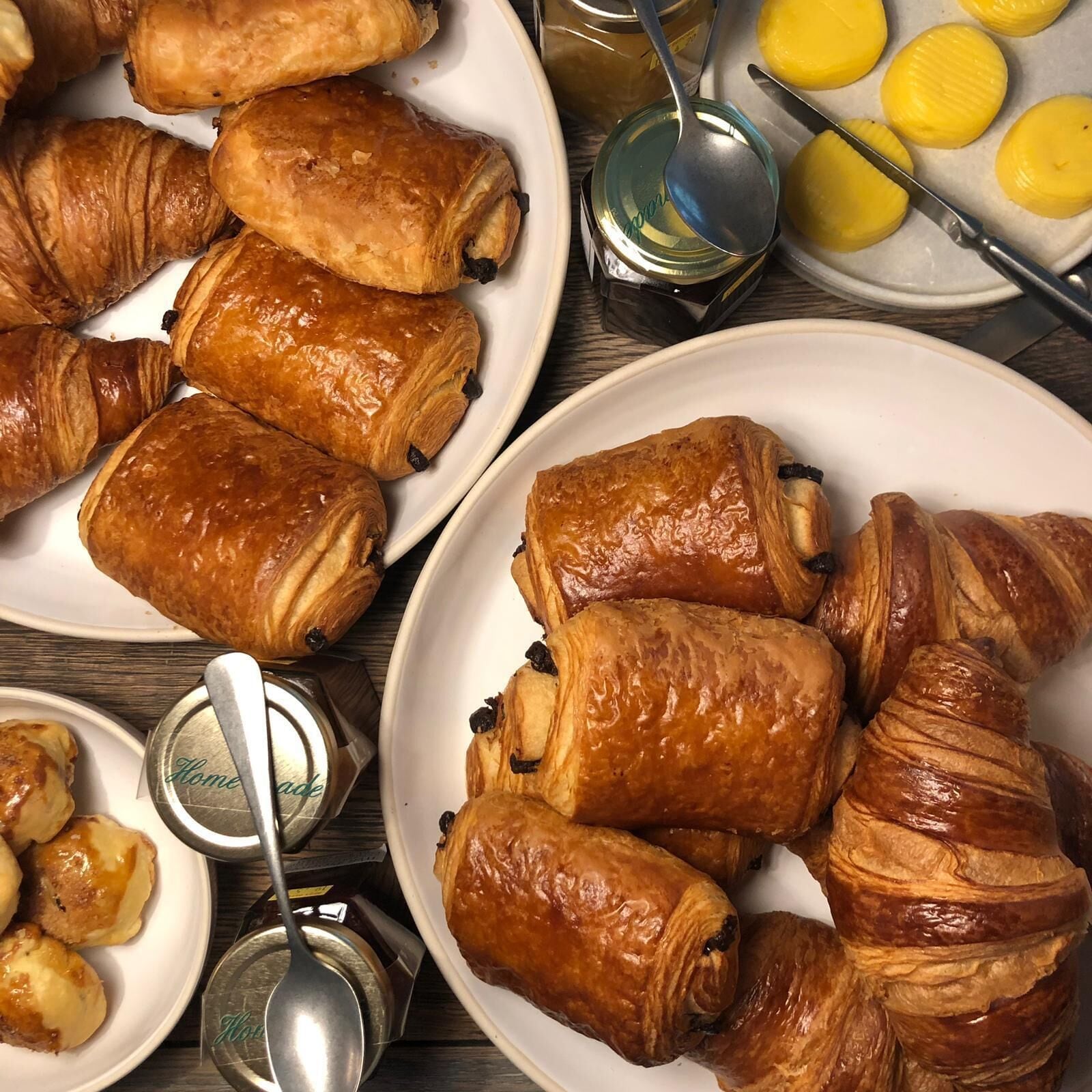 A table with plates of croissants and a jar of jam.