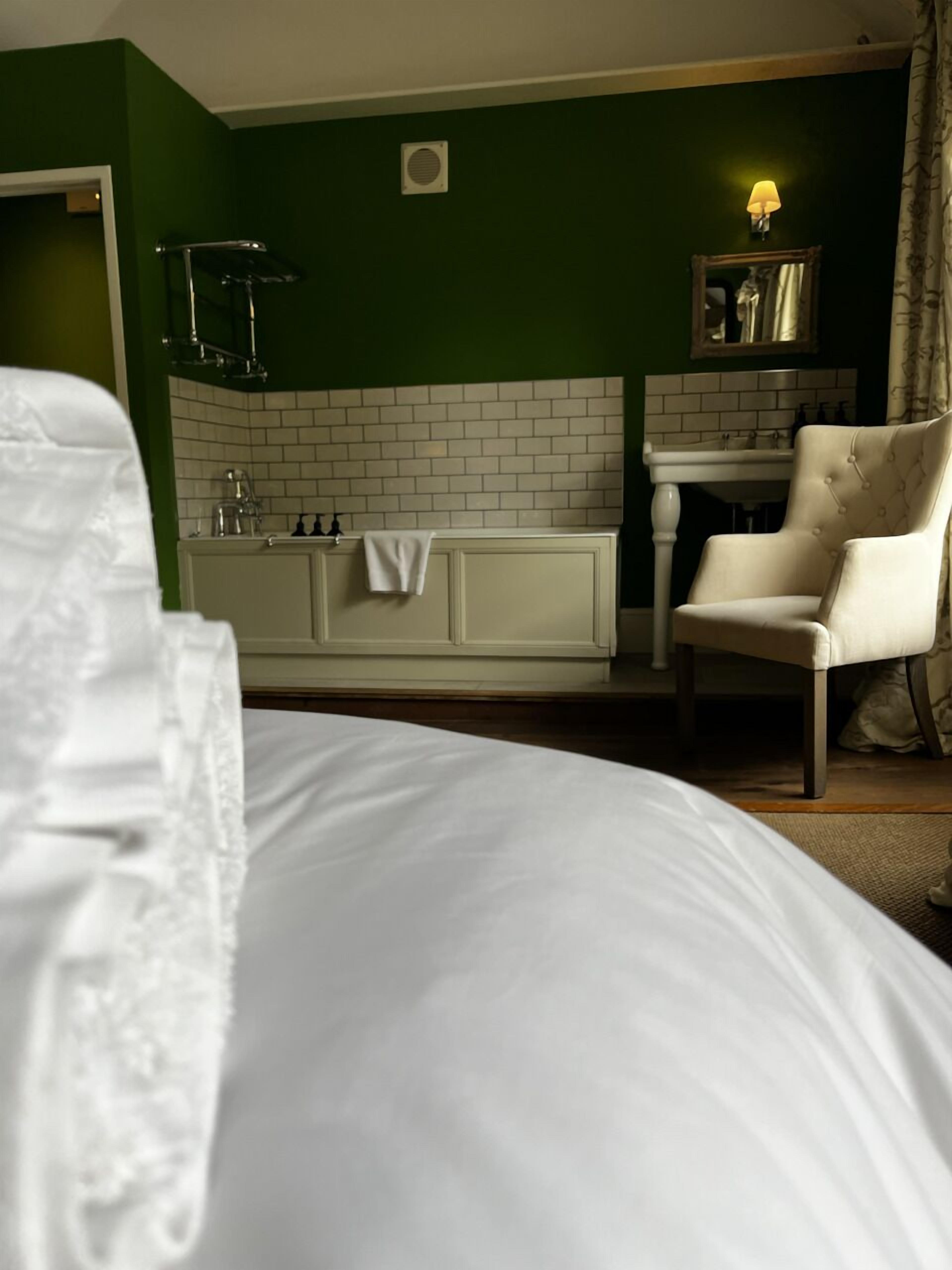 Ein Hotelzimmer mit einem großen Bett, einer weißen Badewanne, einem Sessel und einem kleinen Tisch mit Toilettenartikeln.